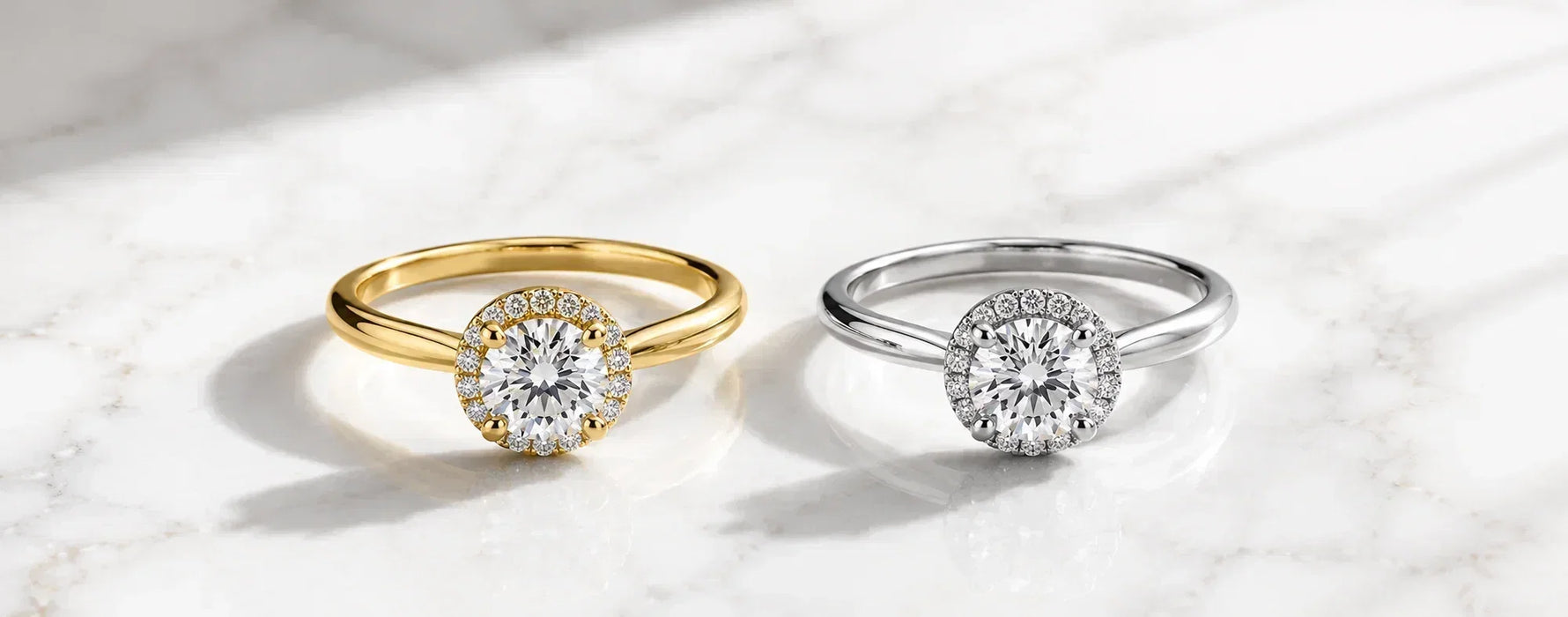 Minimal luxury hero image featuring two identical halo engagement rings in yellow gold and white gold on a white marble background, highlighting the visual difference between popular engagement ring metals.