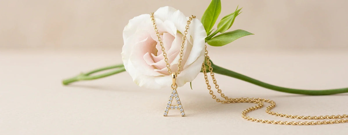 Gold diamond initial A pendant necklace draped over a white lisianthus flower on a cream background