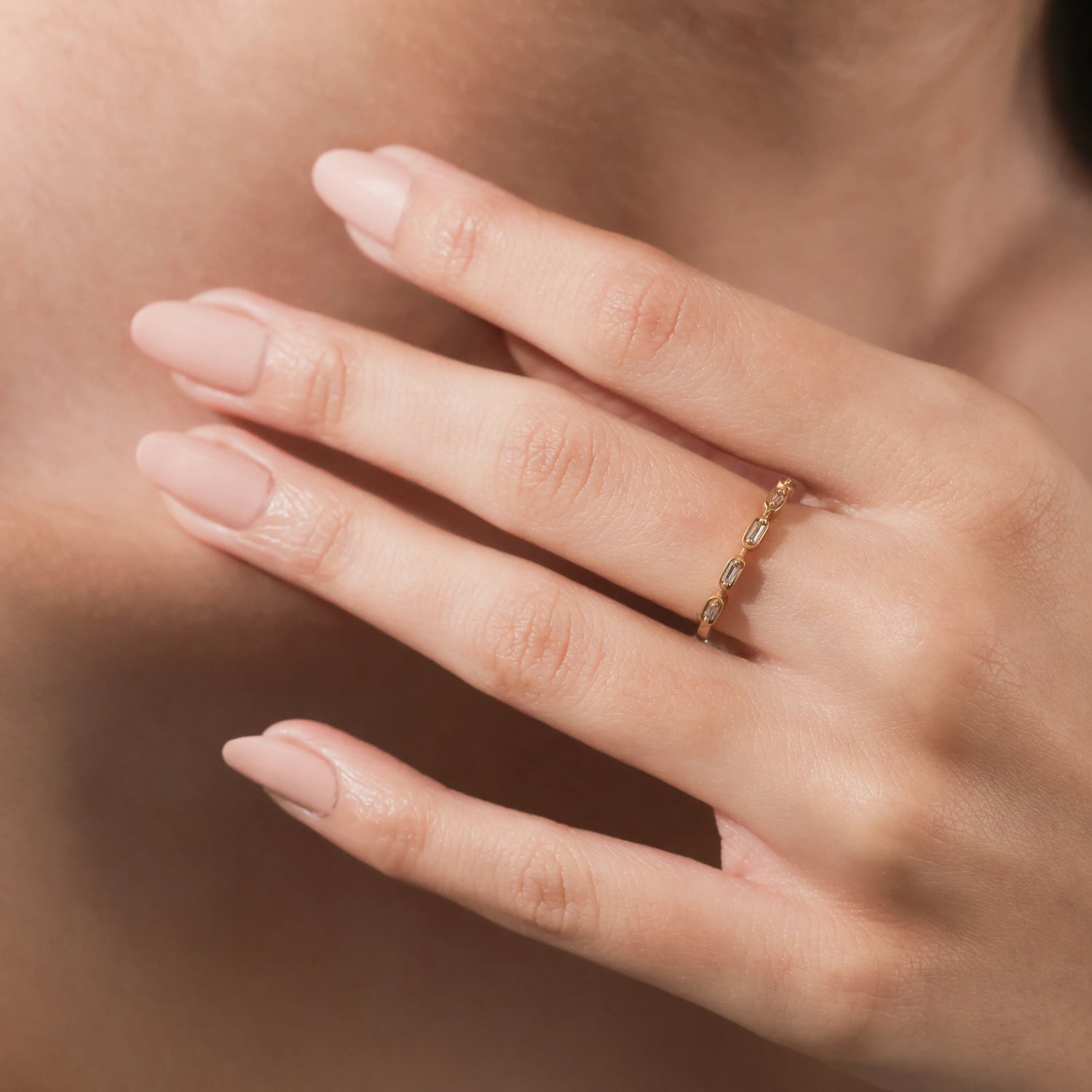 A delicate yellow gold eternity ring featuring an alternating pattern of baguette diamonds worn on a woman's finger.