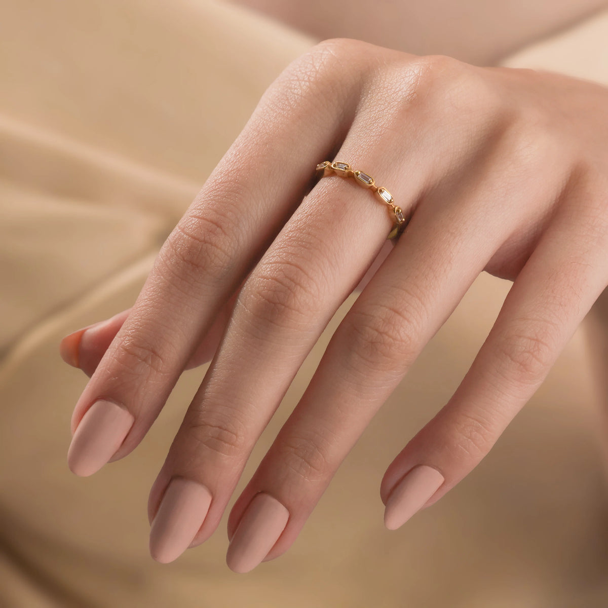 Dainty yellow gold baguette diamond ring with East-West bezel settings, modeled on a hand. Delicate modern fine jewelry wedding band.