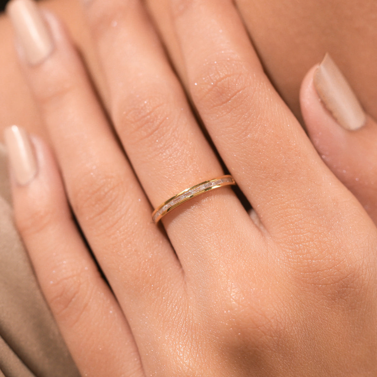 Woman's hand wearing a dainty yellow gold channel set baguette diamond wedding band. A minimal, elegant ring perfect for stacking or everyday wear.