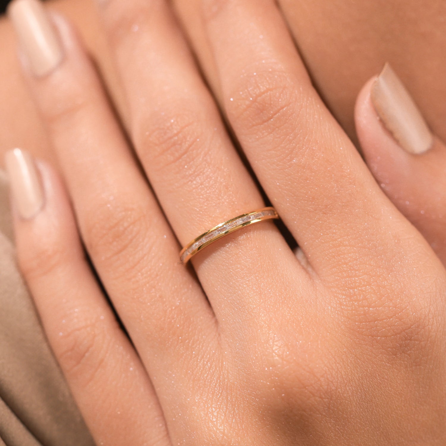 Woman's hand wearing a dainty yellow gold channel set baguette diamond wedding band. A minimal, elegant ring perfect for stacking or everyday wear.