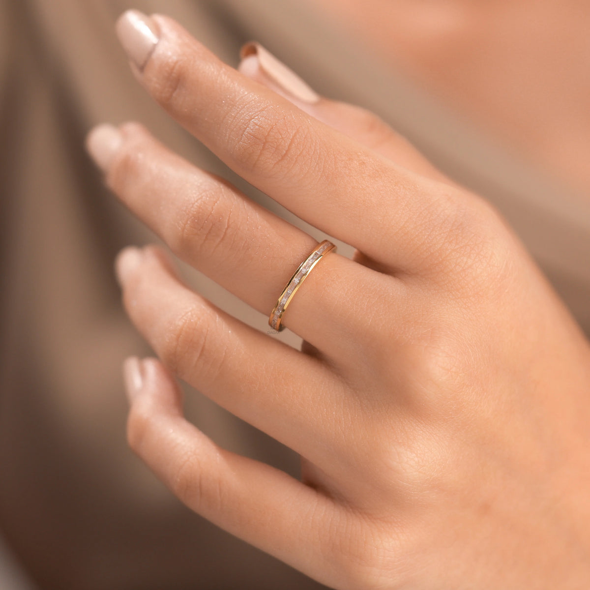 Yellow gold channel set baguette diamond ring worn on a hand. A sleek, modern wedding band or minimalist stacking ring featuring clear baguette diamonds.