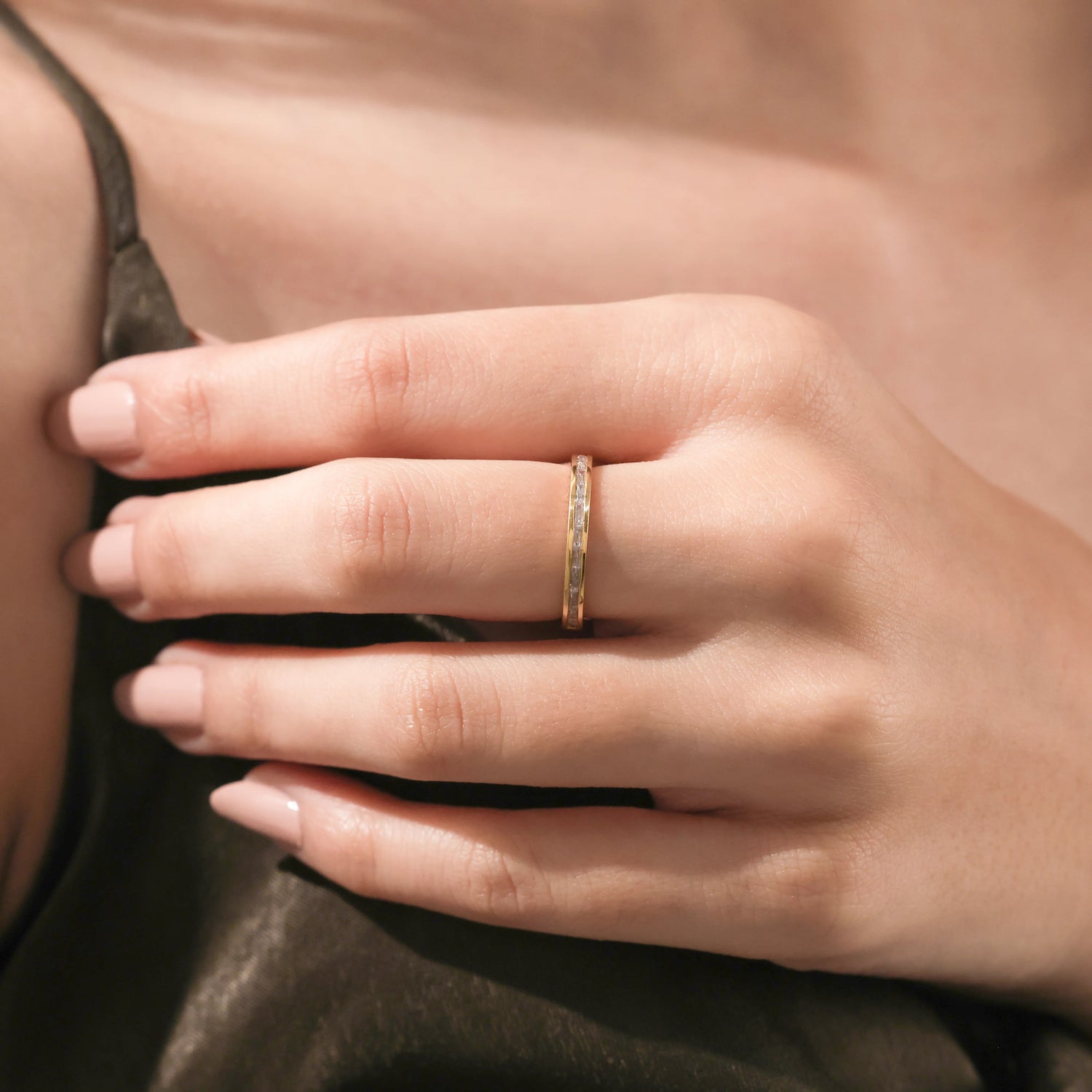 A yellow gold baguette diamond eternity ring worn on a finger as a minimalist lifestyle fine jewelry look, paired with a modern olive green silk dress.