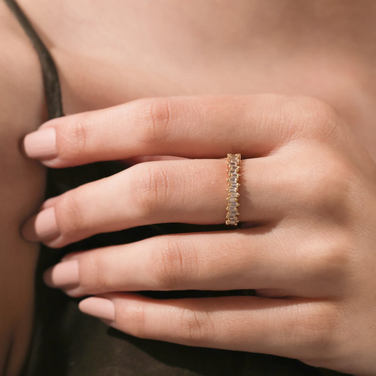 Close-up of a woman's hand with nude nail polish wearing a yellow gold full eternity ring set with baguette cut diamonds on her middle finger.