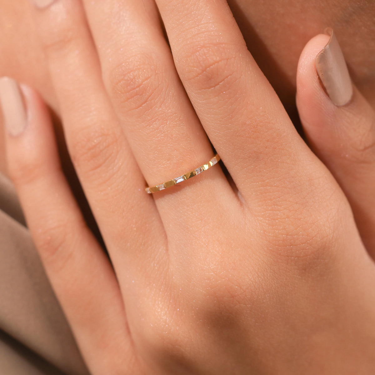 Close-up of a delicate yellow gold band featuring alternating baguette-cut diamonds worn on a woman's finger.