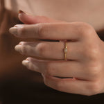 Close up of a minimalist gold promise ring featuring a thin band and baguette diamond wedding band on a hand.