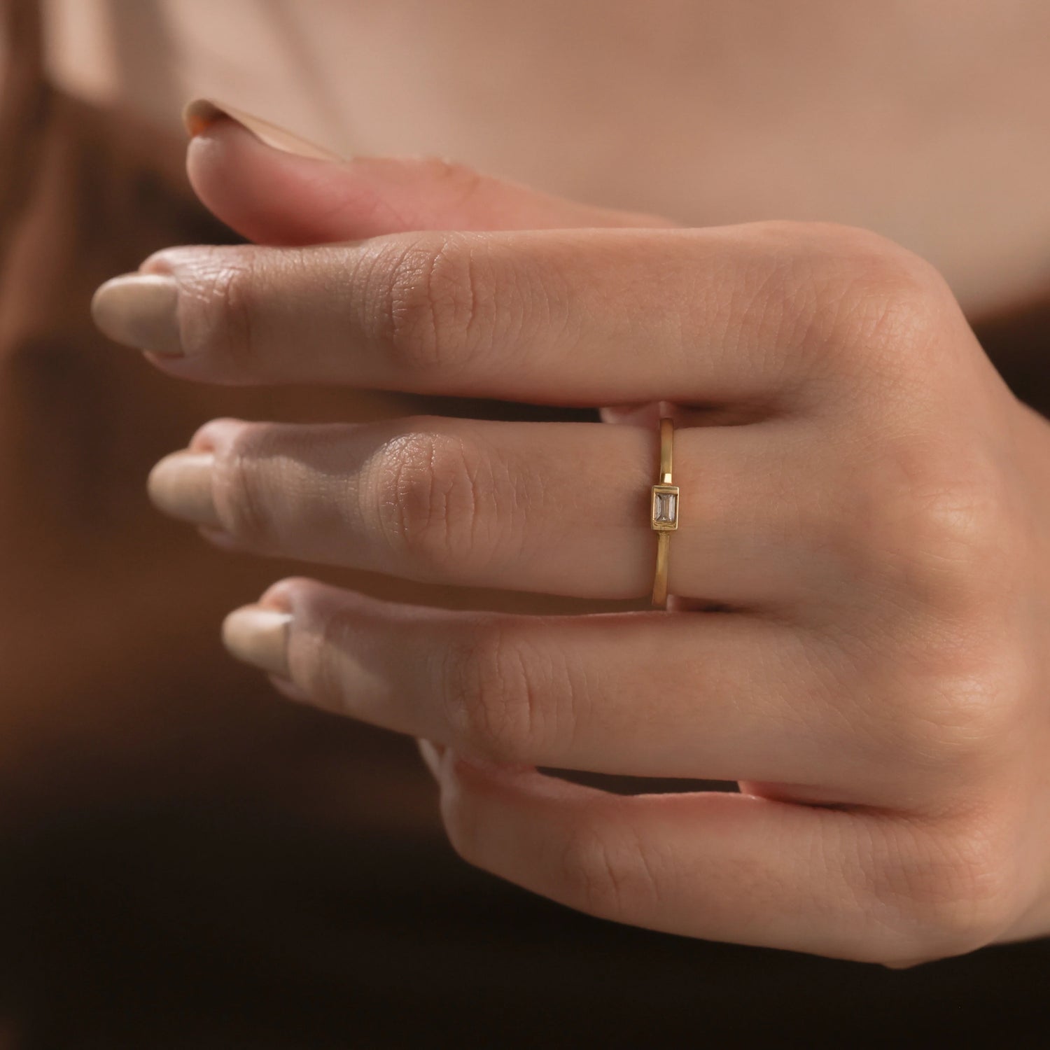 Close up of a minimalist gold promise ring featuring a thin band and baguette diamond wedding band on a hand.