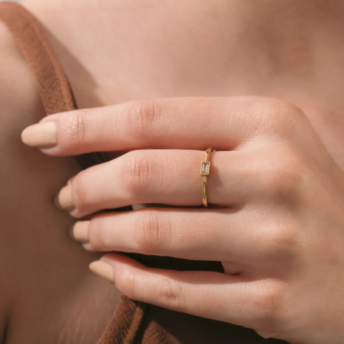 Close-up of a hand wearing a delicate yellow gold band set with a horizontal baguette-cut diamond in a bezel frame.