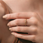 Close-up of a hand wearing a delicate yellow gold band set with a horizontal baguette-cut diamond in a bezel frame.