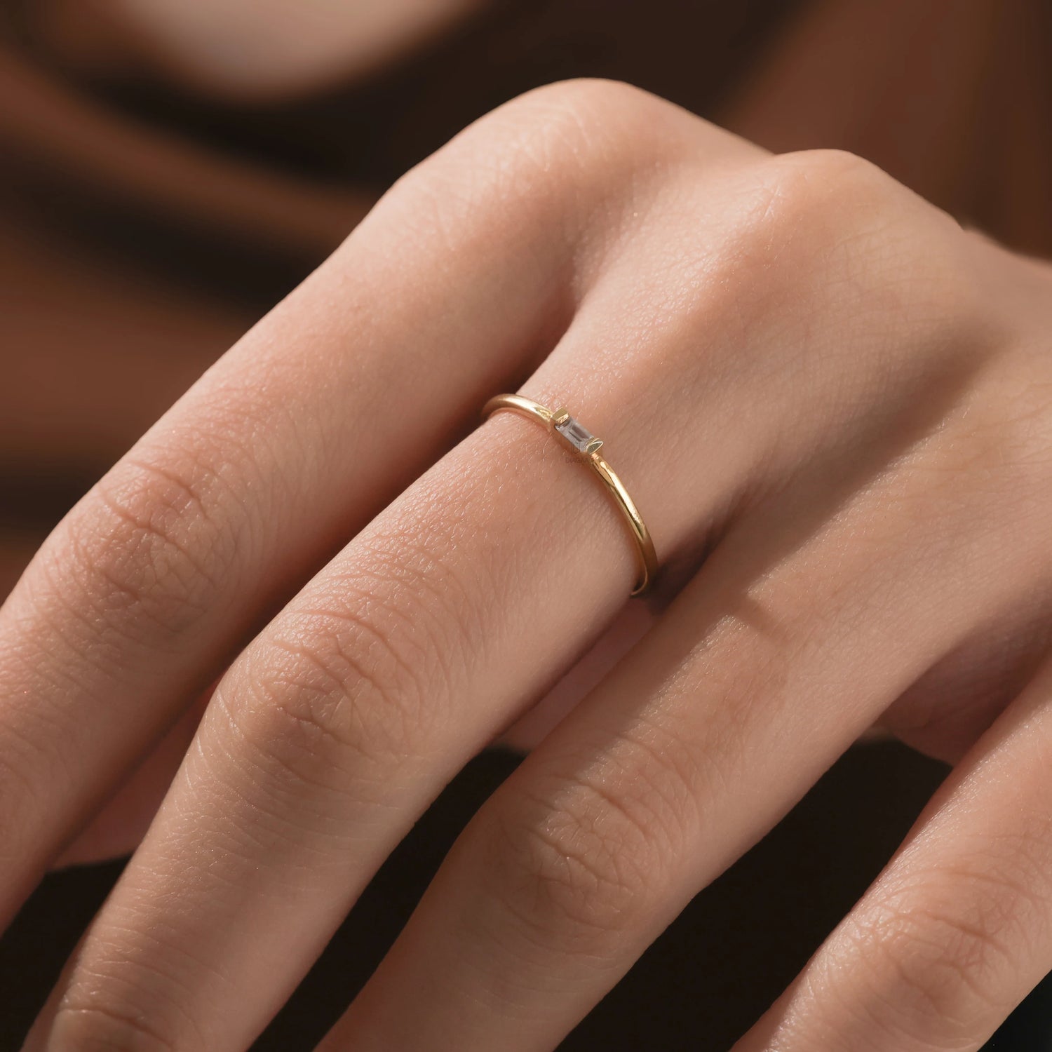 Hand wearing a dainty gold baguette diamond wedding band. This minimalist ring features a single horizontal stone, perfect for stacking.