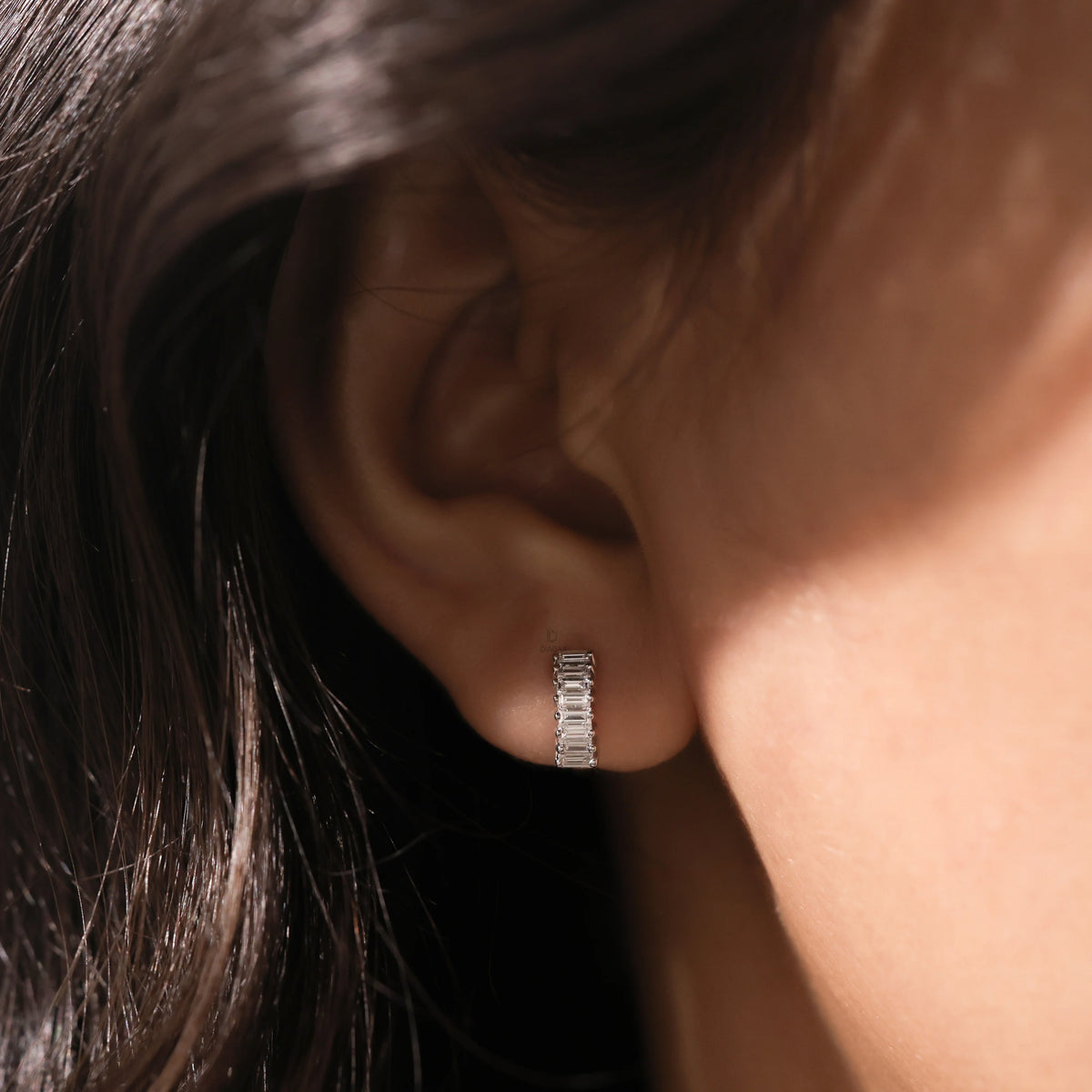 Close-up of a model wearing a delicate white gold baguette diamond huggie hoop earring on her earlobe.