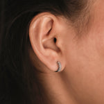 Model wearing a 14k white gold baguette diamond huggie hoop earring in her earlobe piercing, showcasing a stacked horizontal channel-set layout.