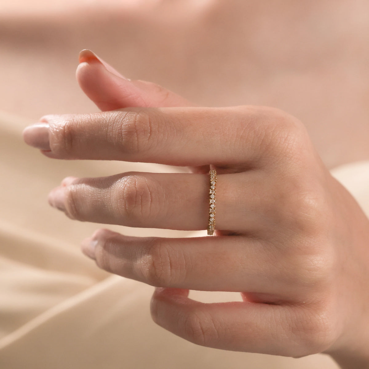 Elegant yellow gold eternity ring with alternating round and rectangular diamonds worn on a finger.