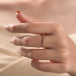 Elegant yellow gold eternity ring with alternating round and rectangular diamonds worn on a finger.