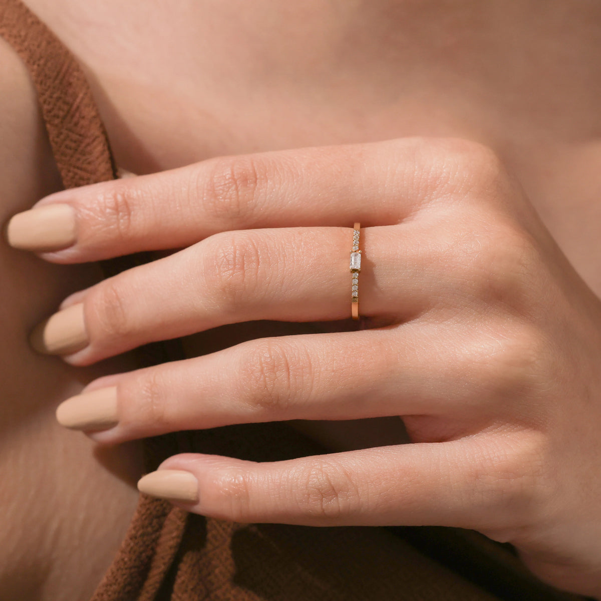 Close-up of a hand wearing a dainty gold ring with a small baguette center diamond and tiny round side stones, showcasing minimalist jewelry style