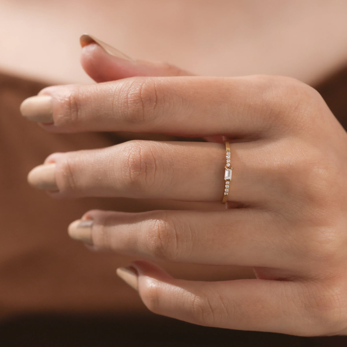 Elegant, thin yellow gold diamond ring with a baguette center stone and sparkling round side diamonds on a hand. Ideal as a delicate promise ring.