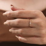 Elegant, thin yellow gold diamond ring with a baguette center stone and sparkling round side diamonds on a hand. Ideal as a delicate promise ring.