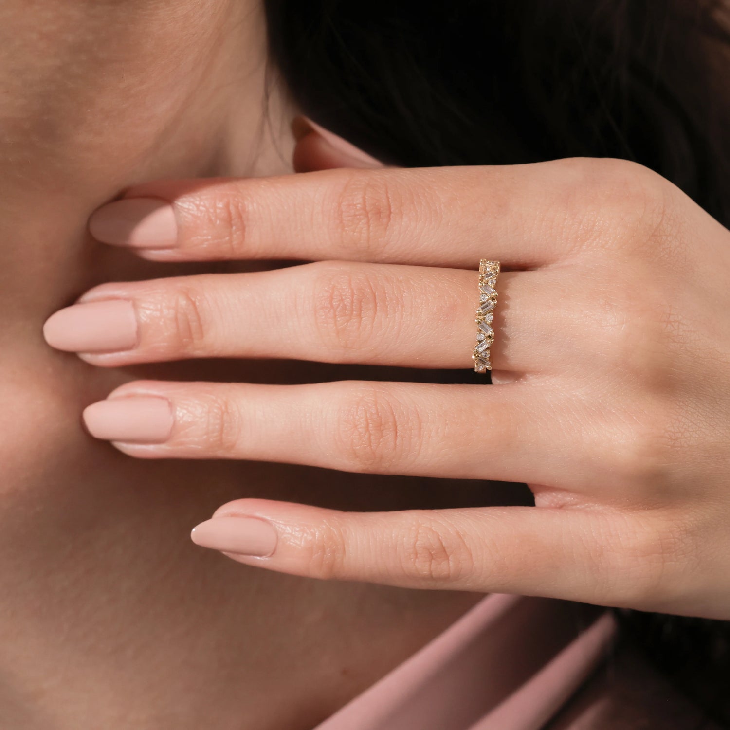 Woman's hand wearing a modern gold diamond ring featuring a staggered pattern of baguette and round cut diamonds. Elegant stacking band.