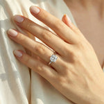 a woman's hand wearing a classic white gold solitaire engagement ring featuring a large brilliant cushion cut diamond on her ring finger.