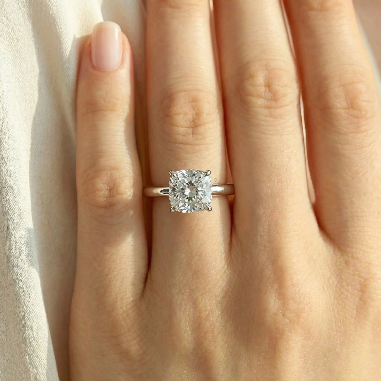 a woman's hand wearing a classic platinum solitaire engagement ring featuring a large brilliant cushion cut diamond on her ring finger.