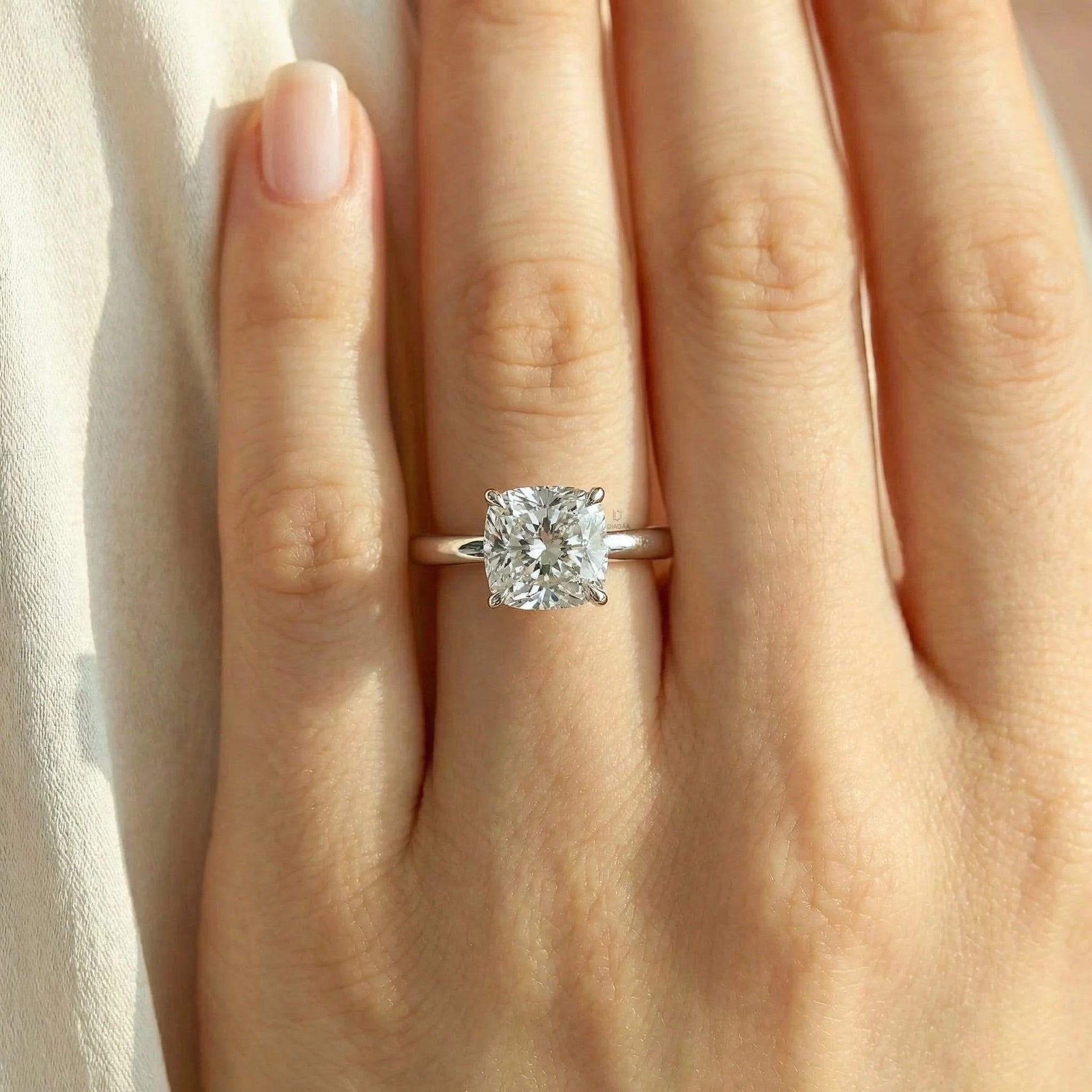 a woman's hand wearing a classic platinum solitaire engagement ring featuring a large brilliant cushion cut diamond on her ring finger.
