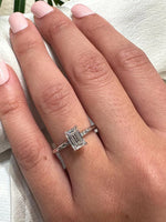 Timeless emerald-cut diamond ring on a hand with a pale pink manicure. Solitaire four-prong setting in white gold against silk fabric.
