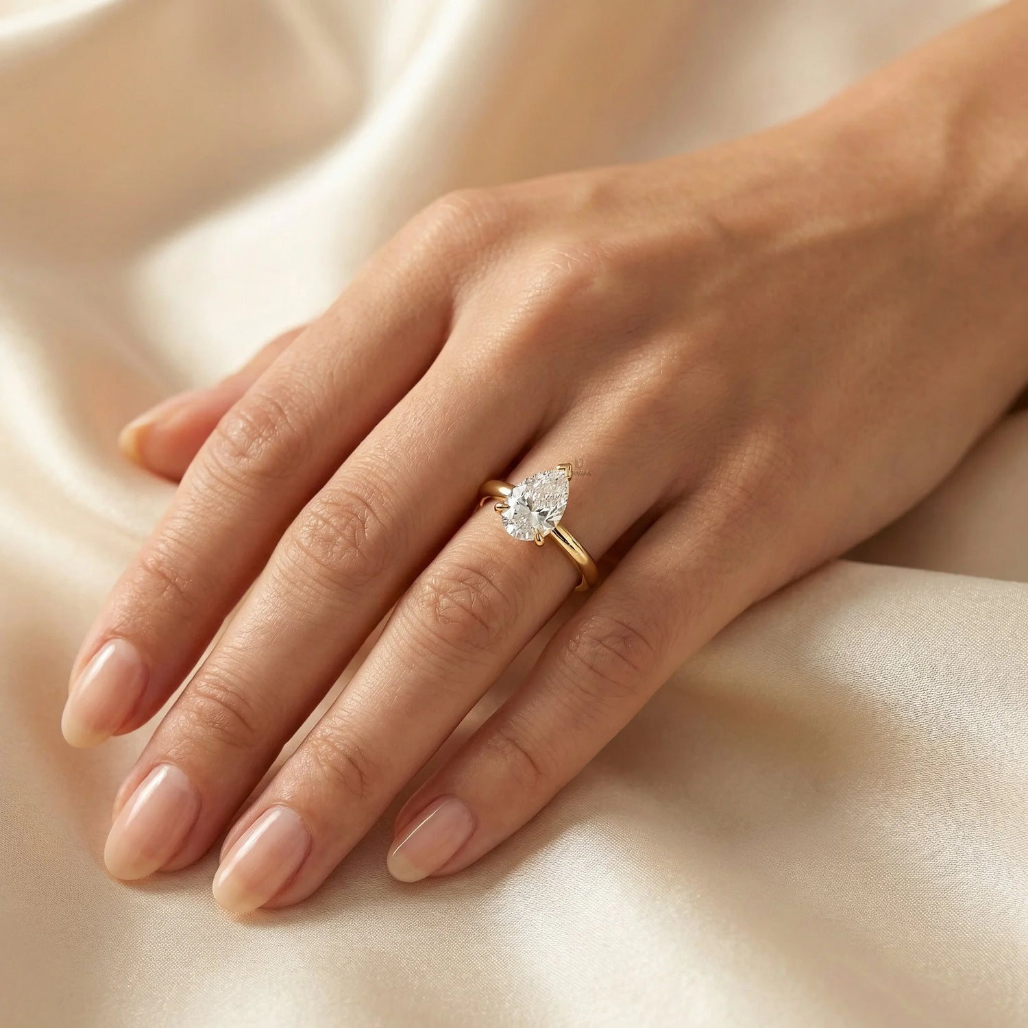 Solitaire pear-cut diamond ring crafted in yellow gold, displayed on a woman's hand resting on soft silk fabric.