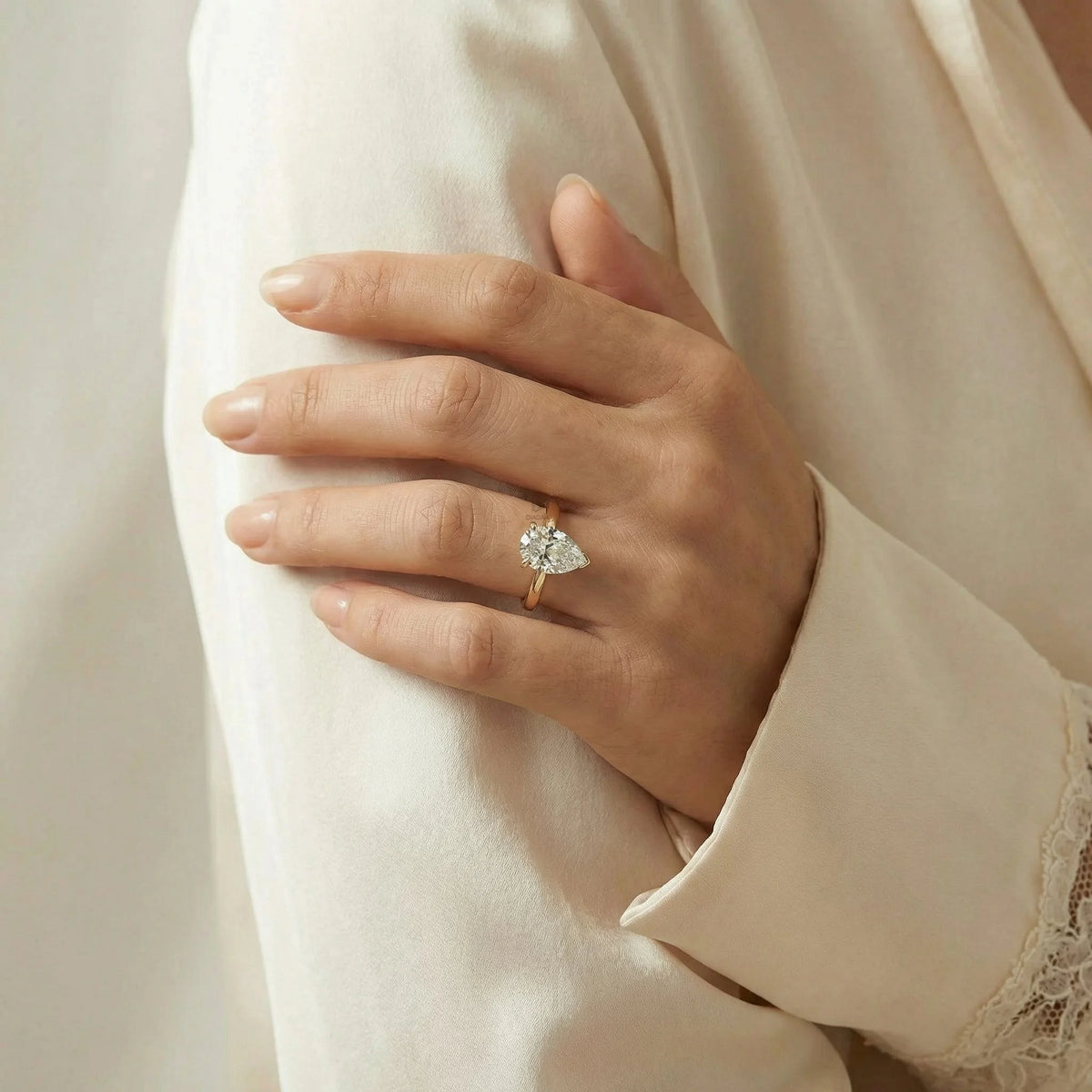 Classic teardrop pear diamond engagement ring with a thin yellow gold band, modeled in a hand.