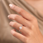 Cushion cut diamond engagement ring in white gold worn on a hand, featuring a brilliant pillow-shaped center stone and a round diamond  pave set side diamond band layout.