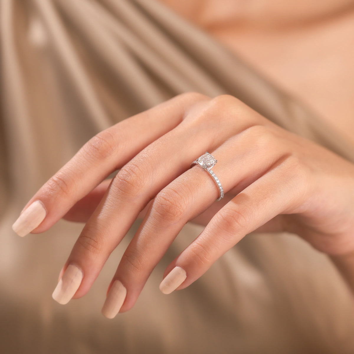 Cushion cut diamond engagement ring in 14k white gold worn on a hand, featuring a brilliant pillow-shaped center stone and a round diamond  pave set side diamond band layout.