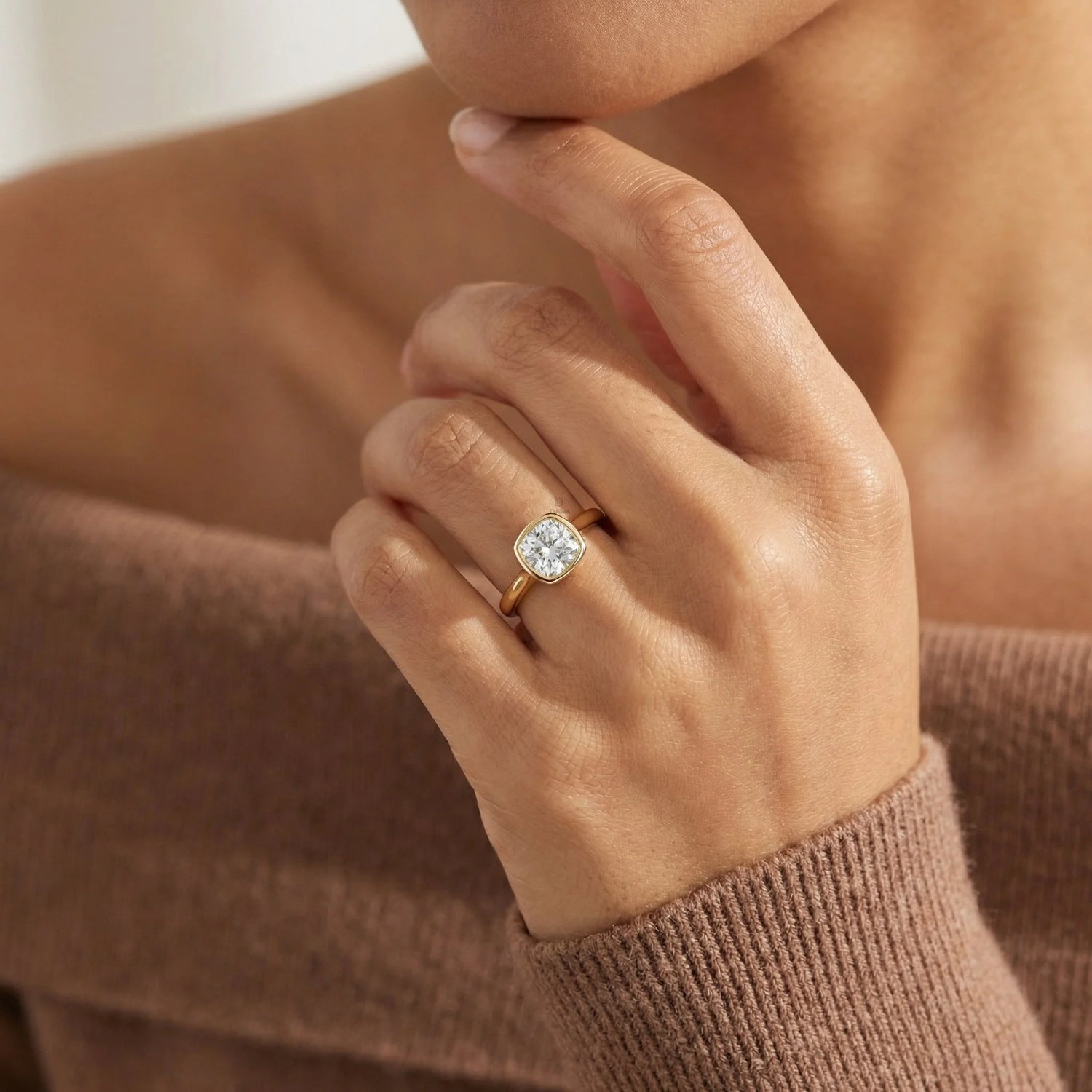 Minimalist yellow gold bezel solitaire ring featuring a square cushion diamond, displayed gracefully on a woman’s finger for a timeless bridal look.