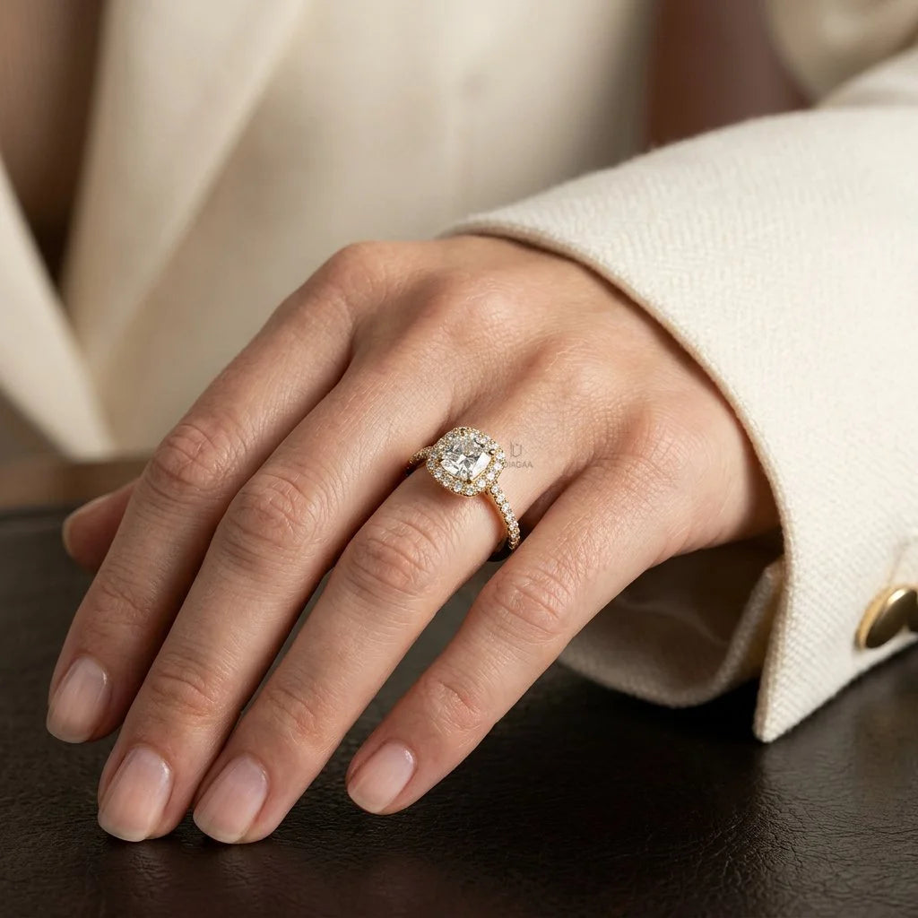 Cushion-cut diamond solitaire halo engagement ring set in 14k yellow gold with a round cut pavé and halo set band, beautifully modeled on a woman's hand.