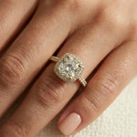 Cushion-cut diamond solitaire halo engagement ring set in yellow gold with a round cut pavé and halo set band, beautifully modeled on a woman's hand.