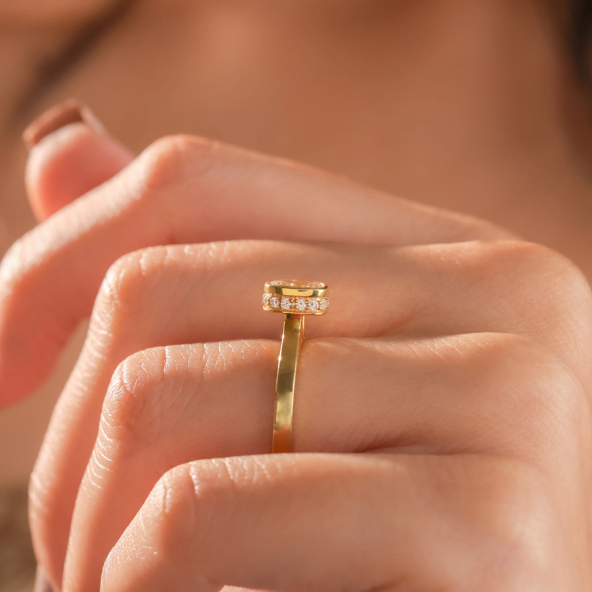 cushion cut diamond engagement ring in yellow gold with a bezel setting and hidden halo on a hand wearing 
