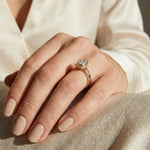 cushion cut diamond solitaire engagement ring in yellow gold with a bezel setting and hidden halo on a hand wearing a white silk shirt.
