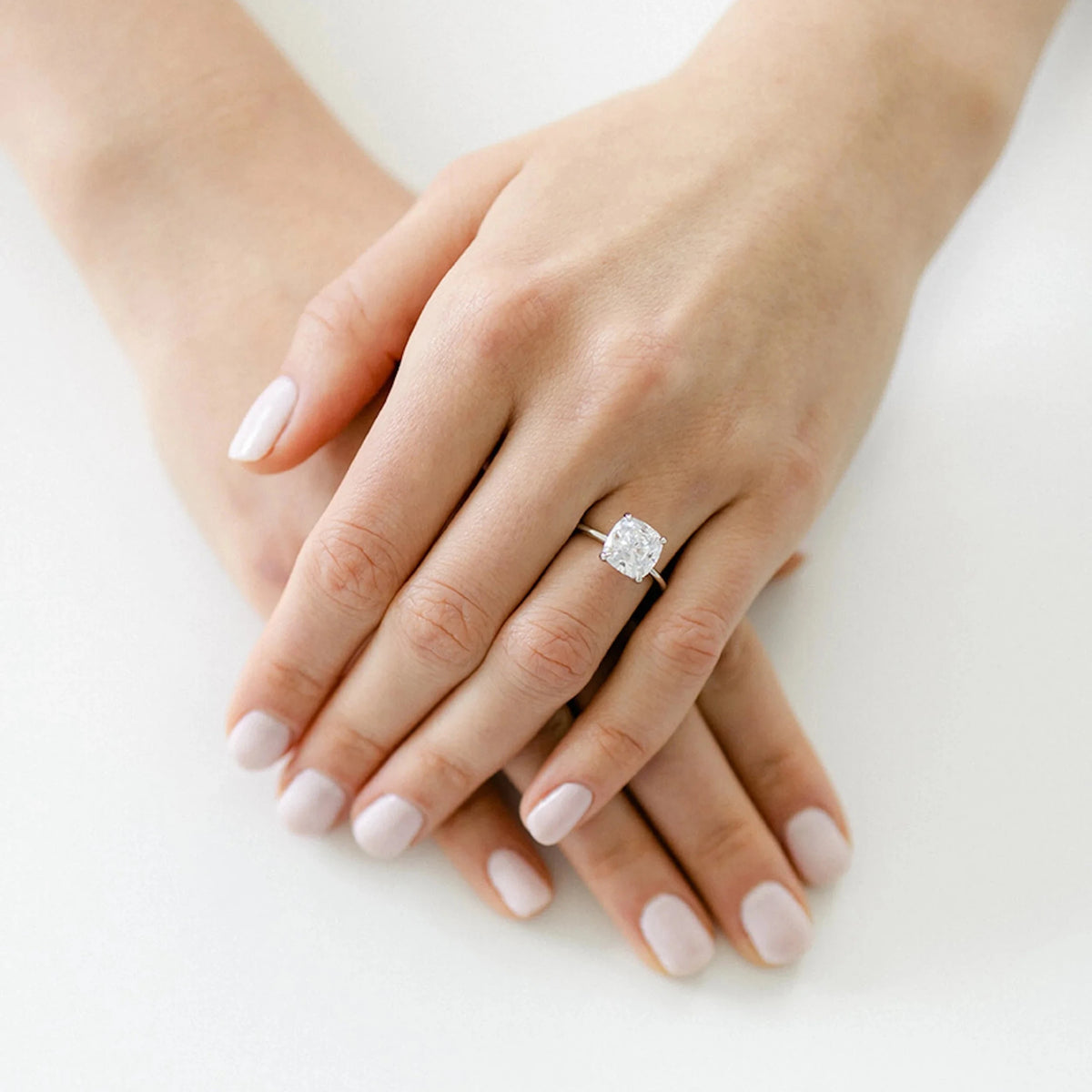A delicate white gold bridal ring showing a clear cushion cut diamond solitaire styled on a hand for a timeless wedding look.