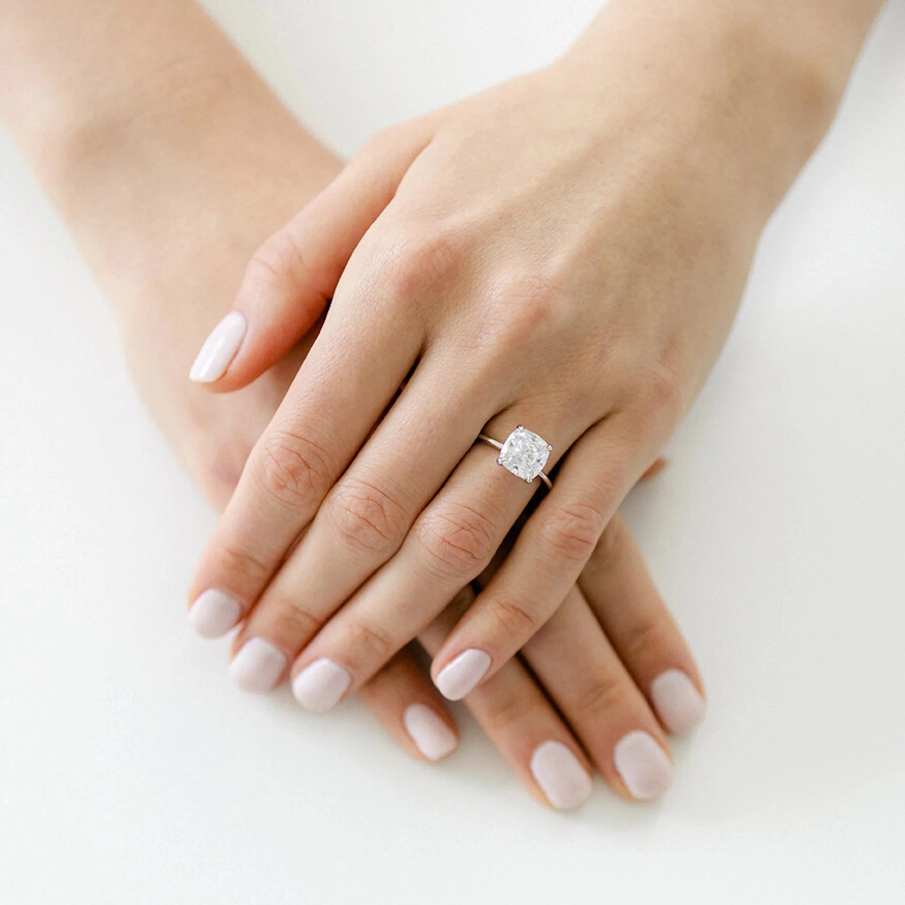 A delicate white gold bridal ring showing a clear cushion cut diamond solitaire styled on a hand for a timeless wedding look.