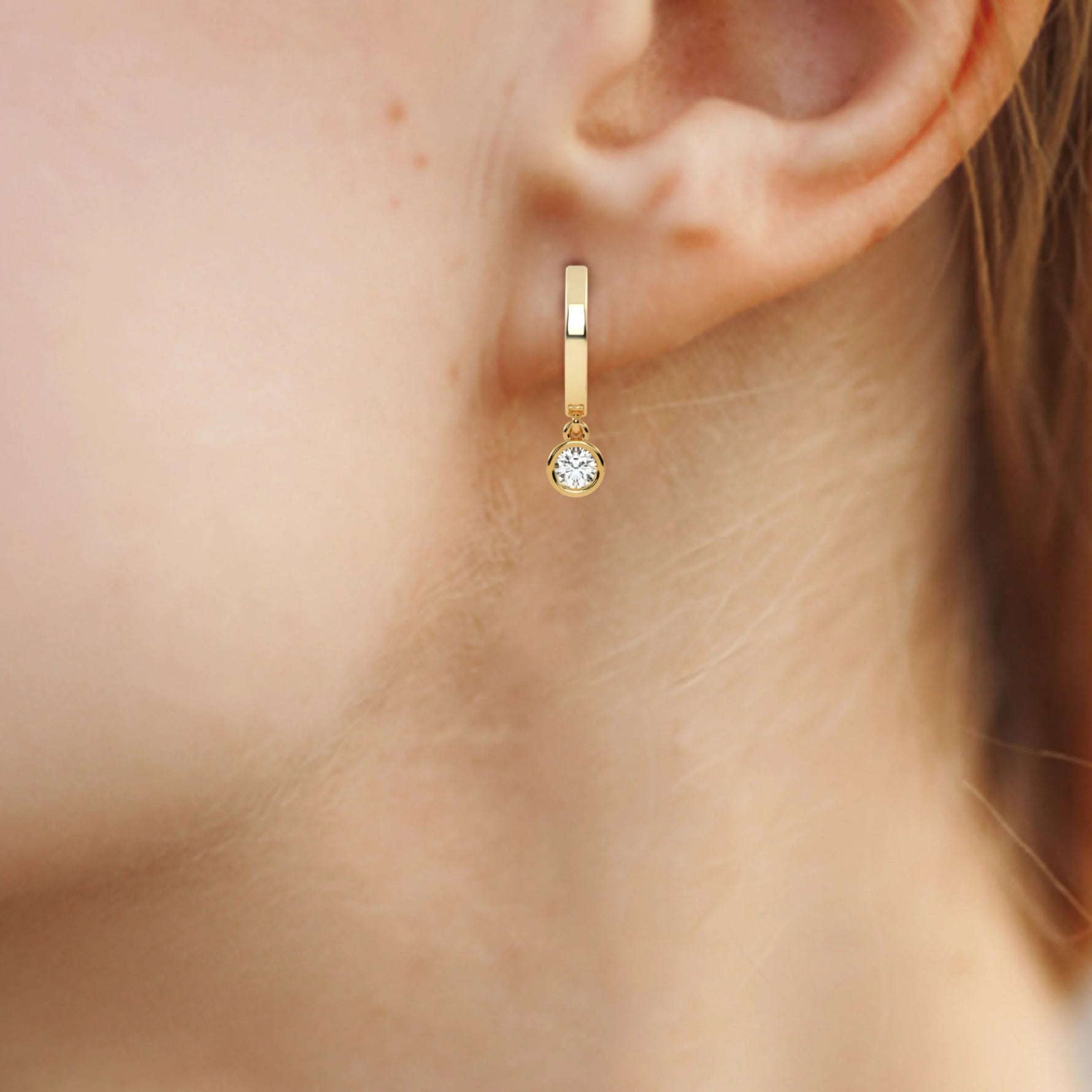 This yellow gold dangling diamond hoop earrings features a moving 0.25 CT diamond on each hoop, securely set in a bezel setting