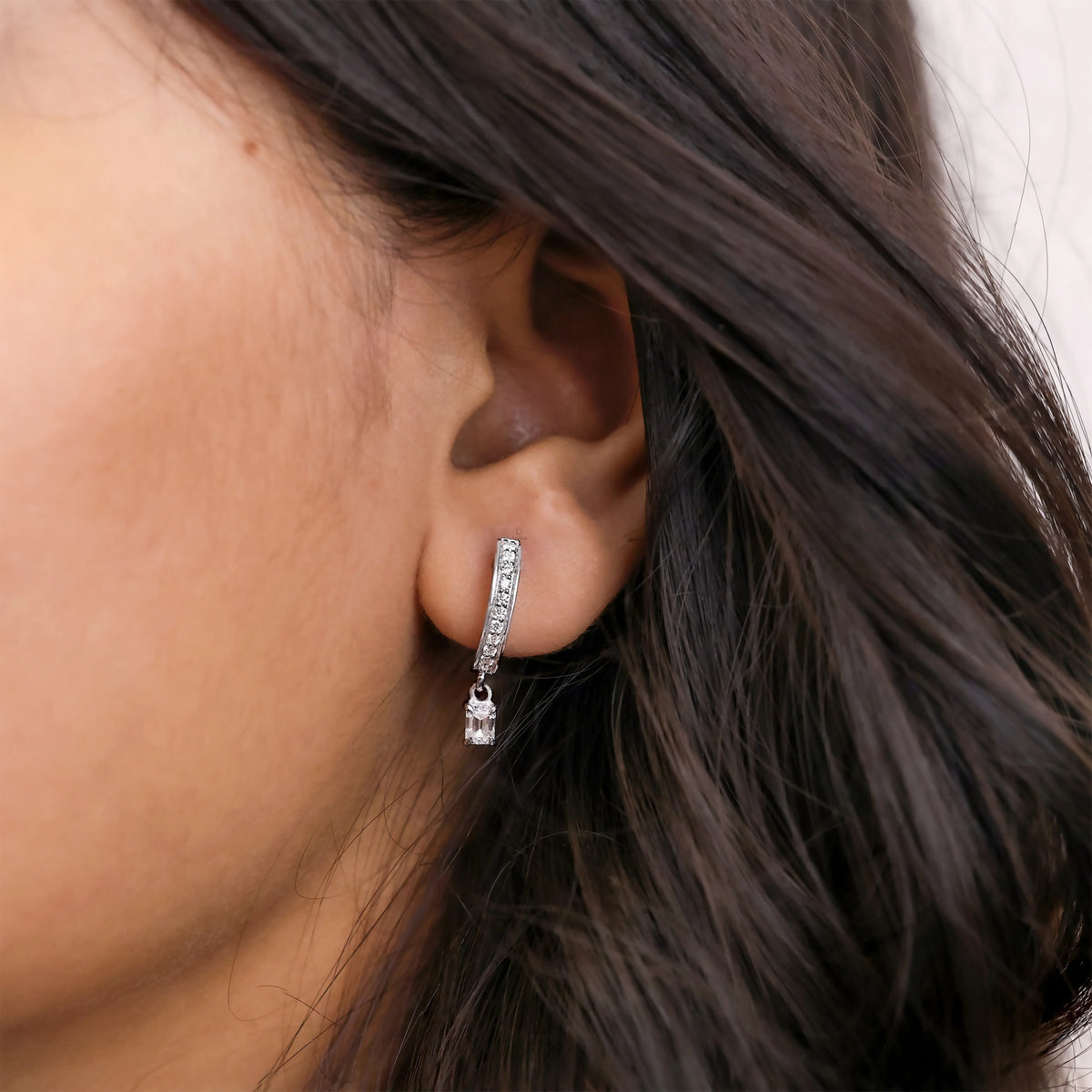  Women wearing round and emerald diamond dangling hoop earring styled on earlobe, shown in 18K white gold with a classic prong setting
