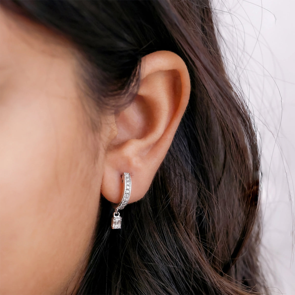 Women wearing round and emerald diamond dangling hoop earring styled on earlobe, shown in 10K yellow gold with a classic prong setting