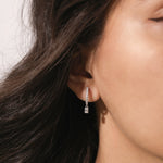Model wearing a round and emerald diamond dangling hoop earring crafted in yellow gold with a delicate prong setting.