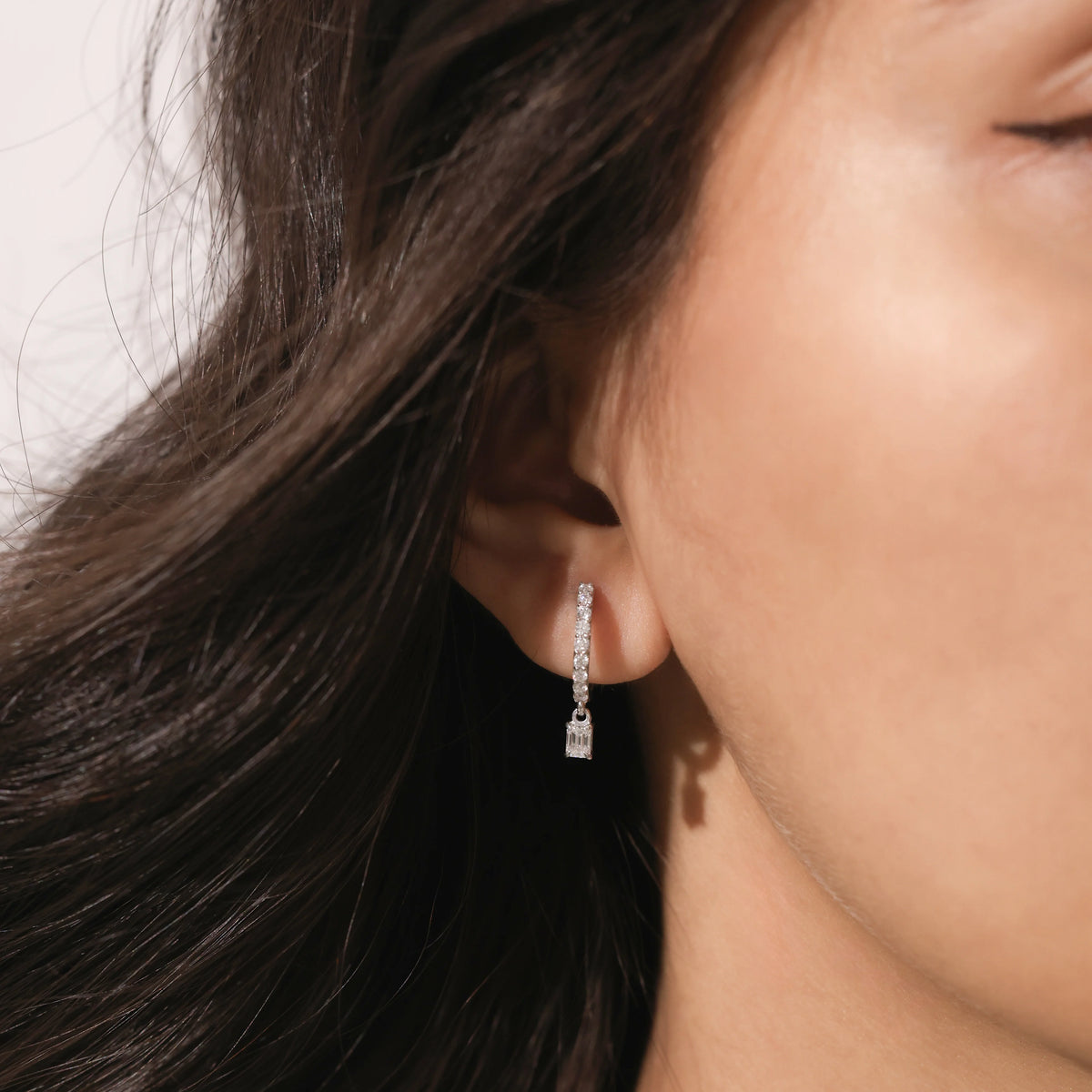 Model wearing a round and emerald diamond dangling hoop earring crafted in yellow gold with a delicate prong setting.