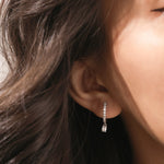 Model wearing a round and emerald diamond dangling hoop earring crafted in yellow gold with a delicate prong setting.