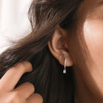 Model wearing a round and emerald diamond dangling hoop earring crafted in yellow gold with a delicate prong setting.