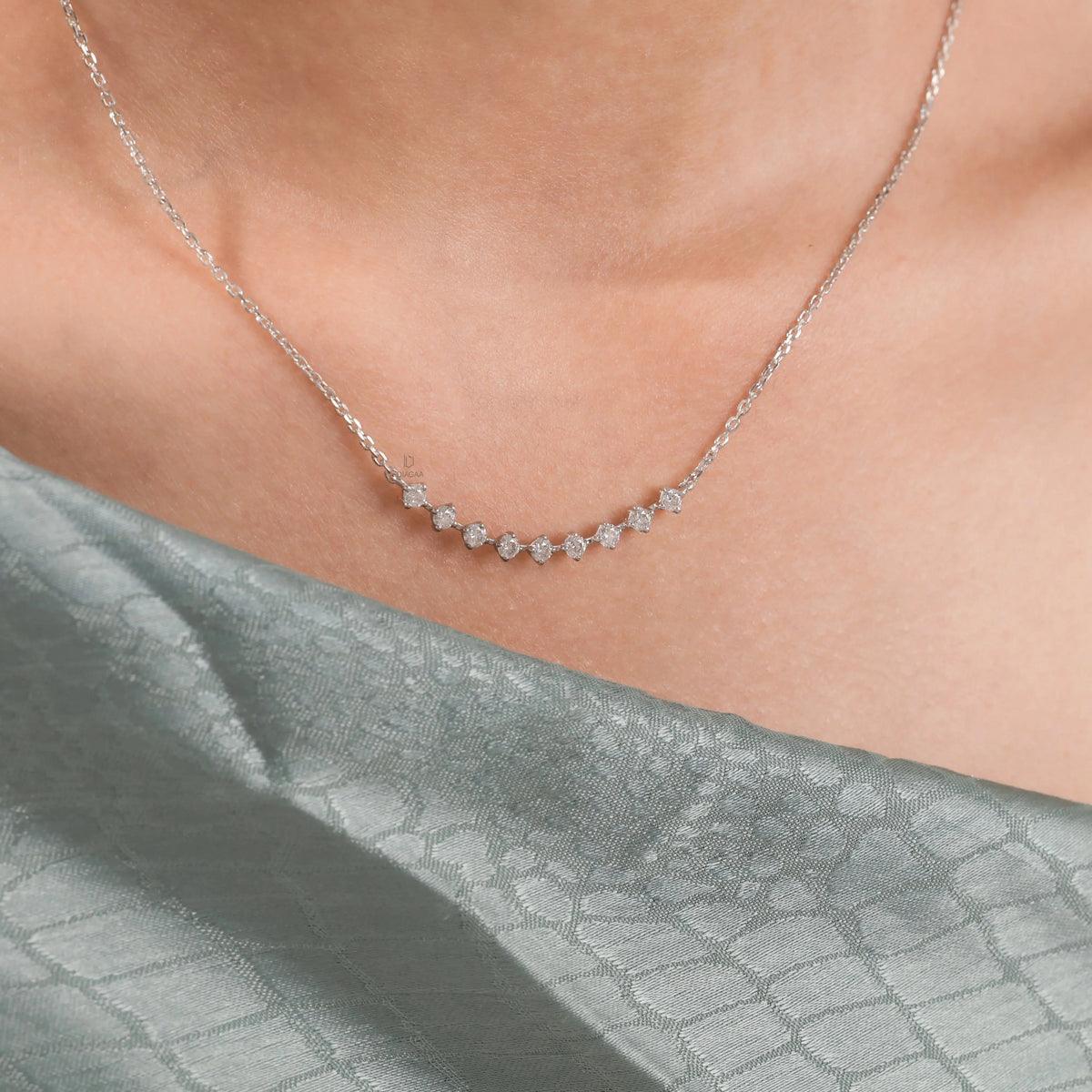 Close-up of a delicate curved bar round diamond necklace with prong-set stones, elegantly styled on a model in beautiful 18K yellow gold.