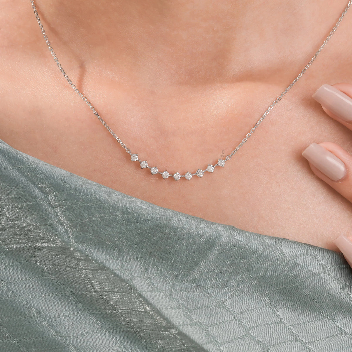Close-up of a delicate curved bar round diamond necklace with prong-set stones, elegantly styled on a model in beautiful 14K yellow gold.