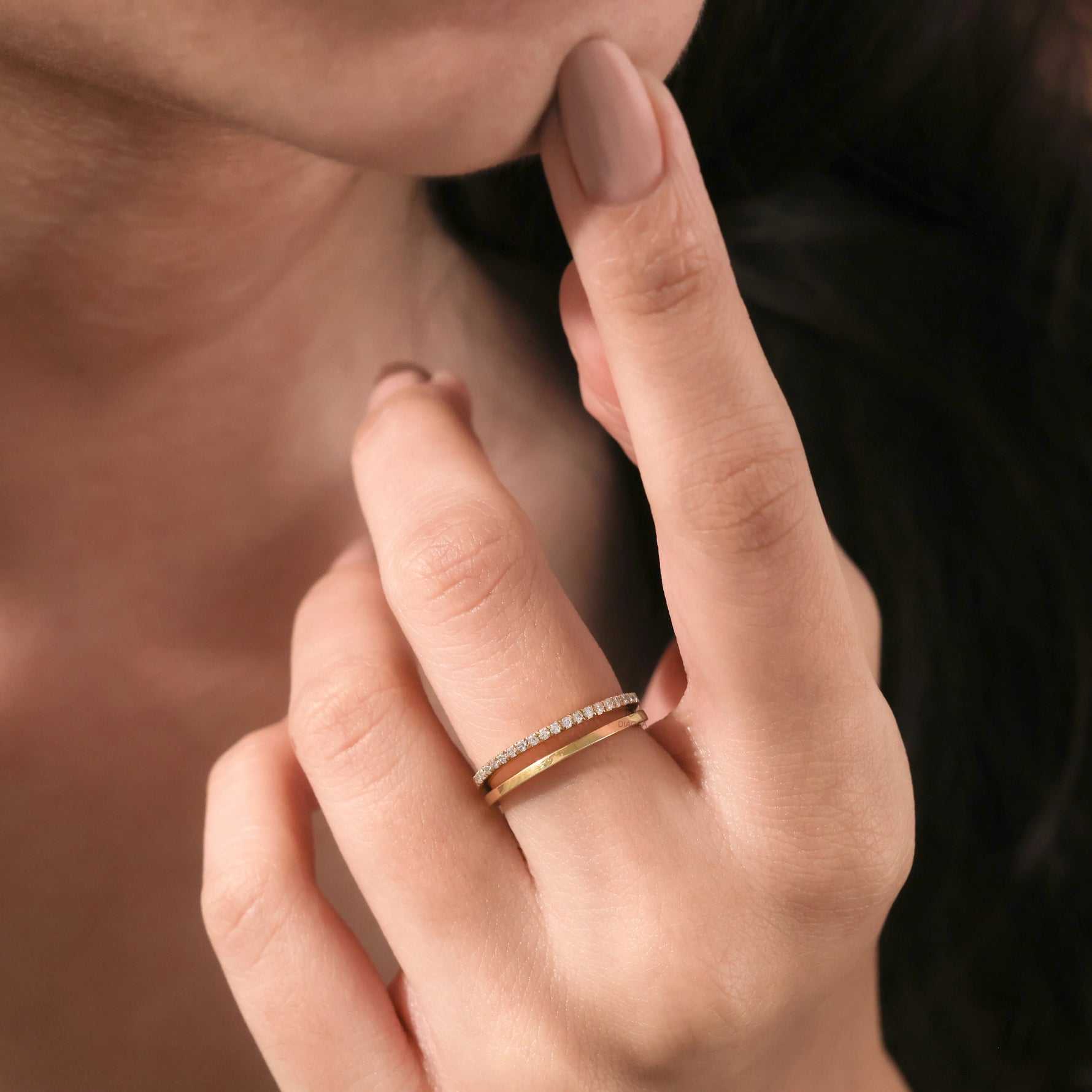 Close-up of a woman's hand wearing a delicate yellow gold double band ring featuring one plain and one pave diamond band.