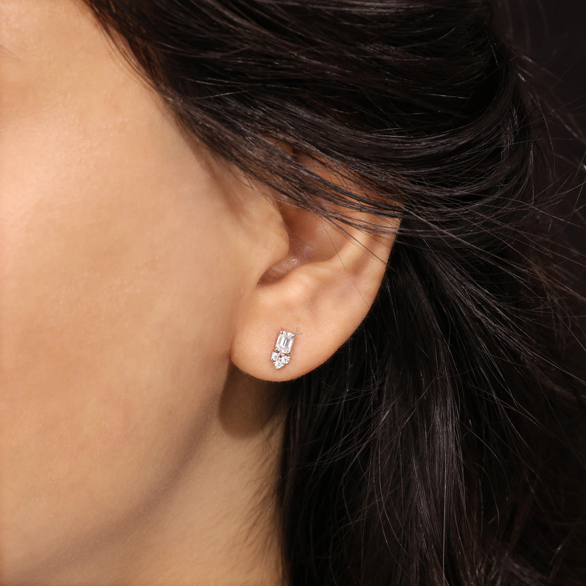 Model wearing an elegant cluster-style emerald and round diamond stud earring with a prong setting in yellow gold.