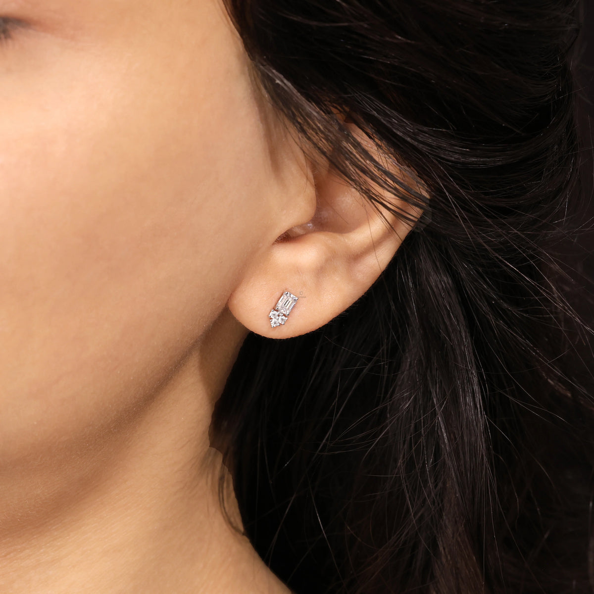 Model wearing an elegant cluster-style emerald and round diamond stud earring with a prong setting in yellow gold.